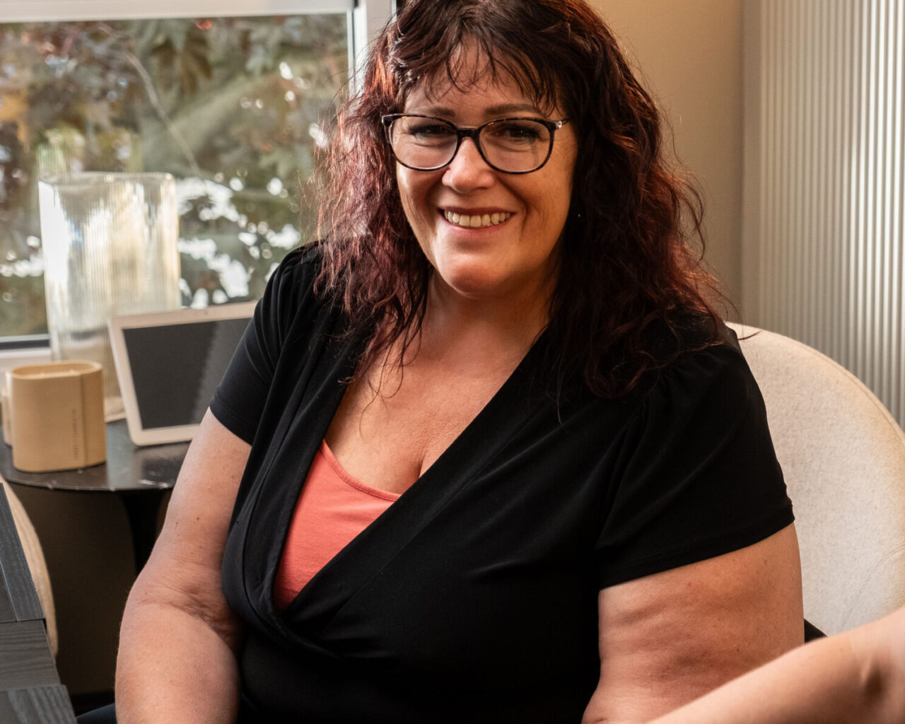 'http://Two%20people%20sitting%20indoors,%20smiling%20and%20talking.%20The%20woman%20on%20the%20left%20has%20curly%20dark%20hair%20and%20glasses,%20wearing%20a%20black%20top%20with%20an%20orange%20shirt%20underneath.%20The%20man%20on%20the%20right%20wears%20scrubs,%20glasses,%20and%20a%20black%20cap.