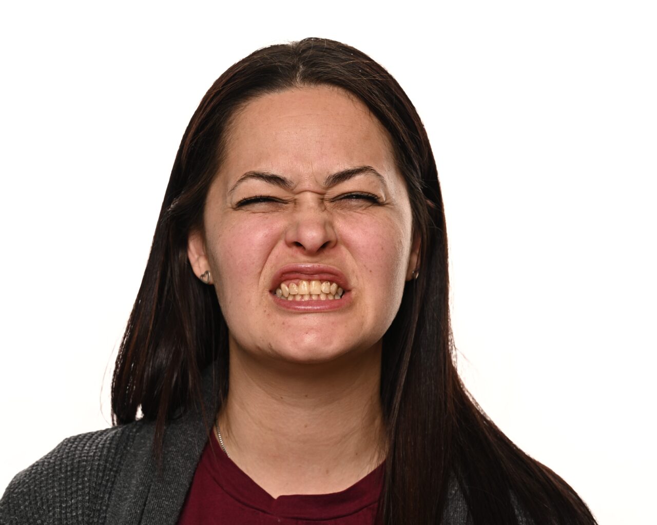 'http://A%20woman%20with%20long%20dark%20hair%20grimaces,%20scrunching%20her%20nose%20and%20baring%20her%20teeth,%20showing%20an%20expression%20of%20discomfort%20or%20irritation.%20She%20is%20facing%20the%20camera%20against%20a